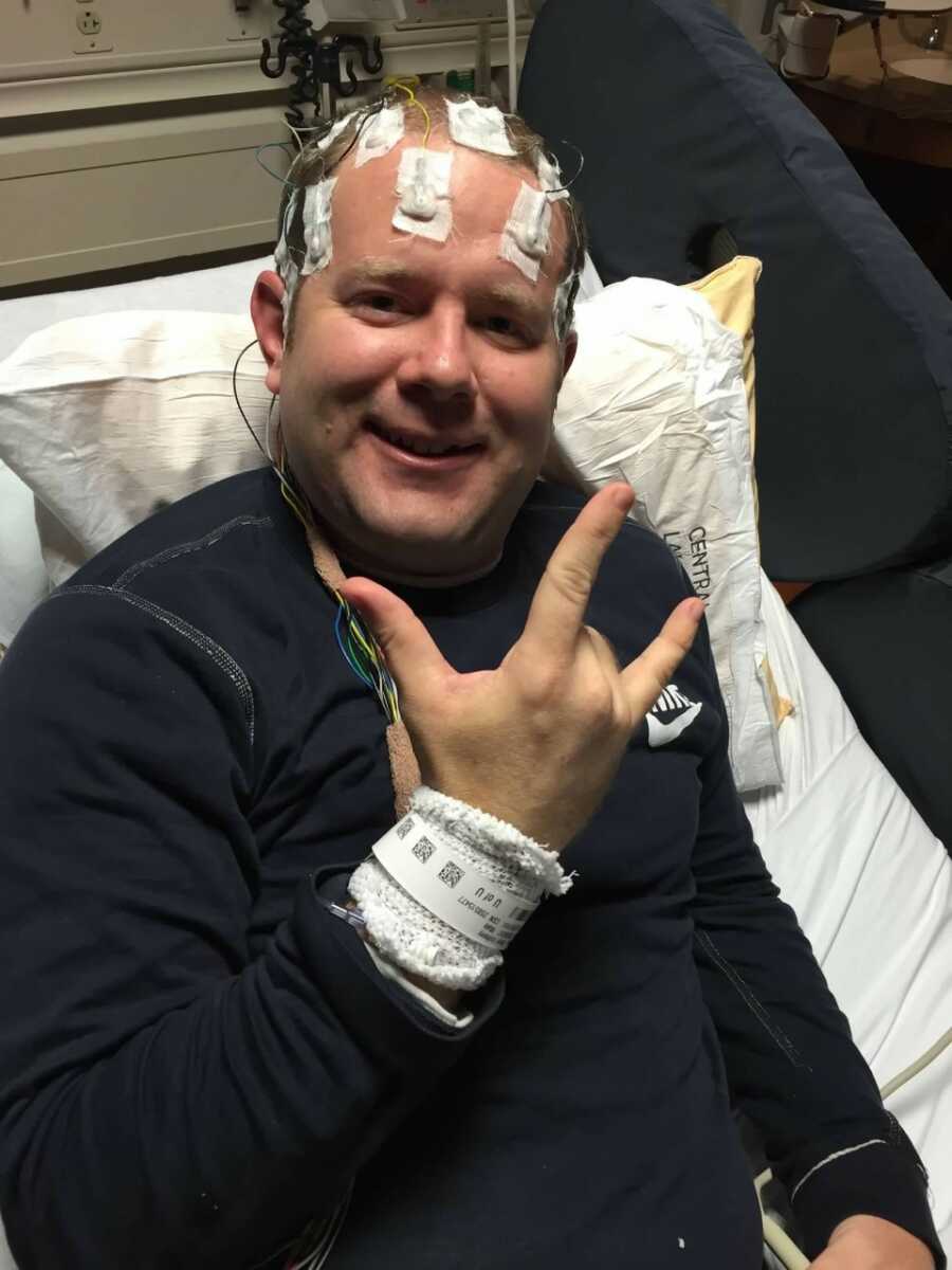 Father battling brain cancer sits in hospital bed and signs "I love you" while hooked up to electrodes on his head.