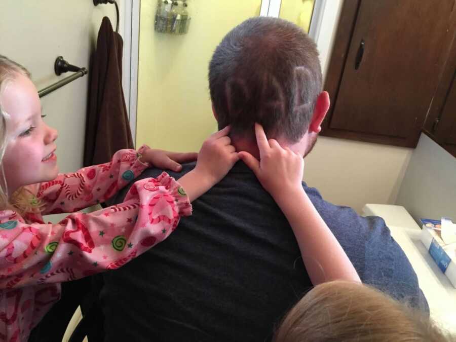 Young girls trace the word "dad" shaved into the back of their father's head.