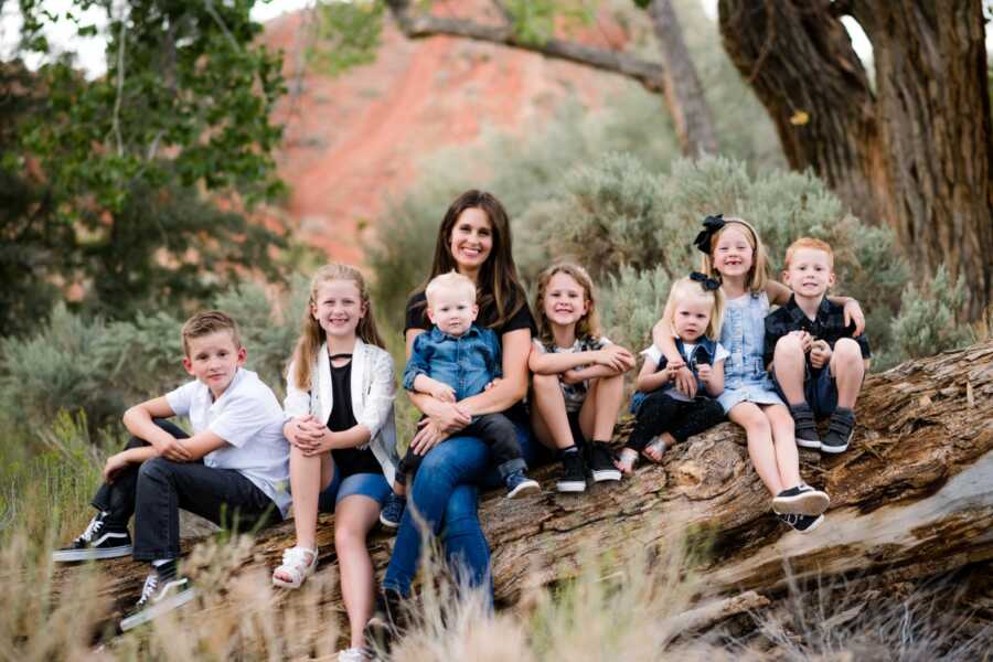 Young widow sits on fallen tree for family picture with her seven children.