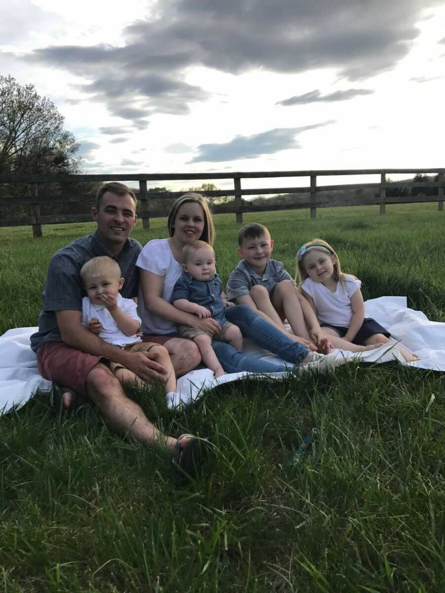 Young couple with four children take picture sitting on blanket in the grass in the evening.