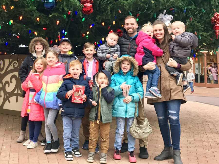 Parents with their 11 children stand in front of outdoor Christmas tree.