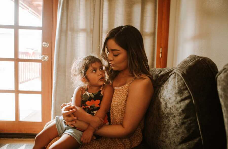 mom holds her daughter on her lap, looking down at her