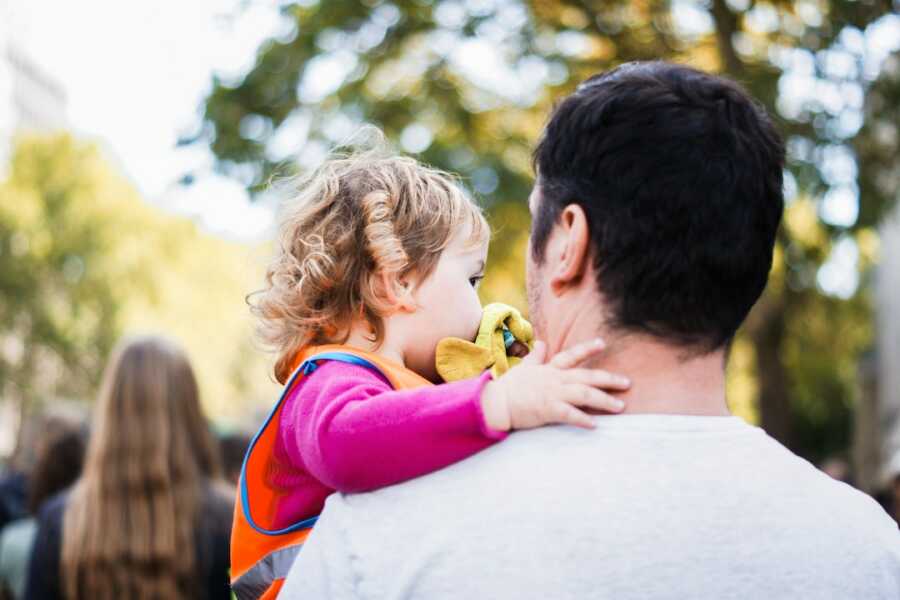 dad holds daughter, mom is walking in distance