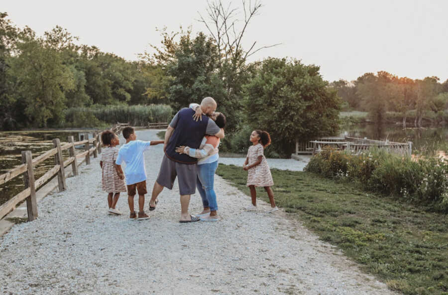 Domestic abuse survivor holds and kisses husband on rock trail surrounded by three kids