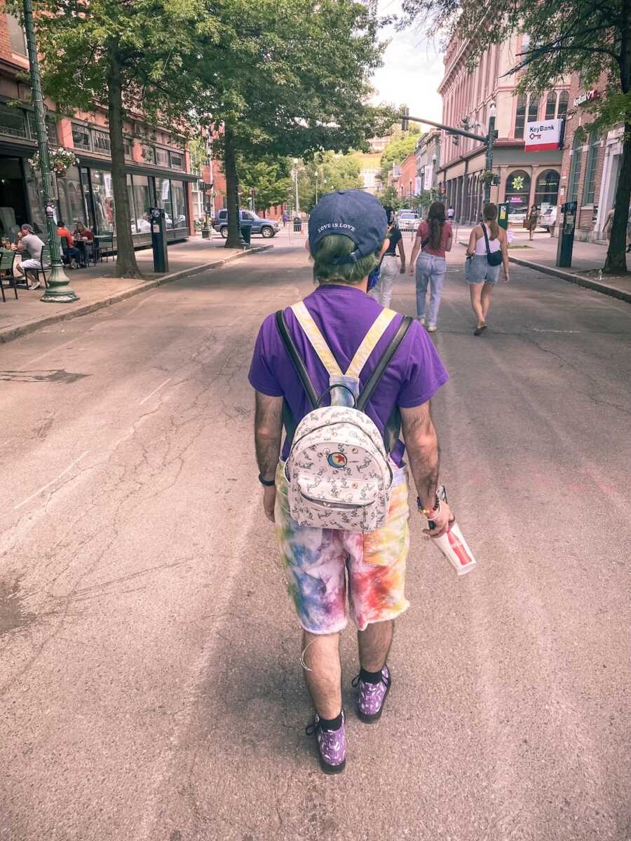 a man wearing a backpack walking down a street at Pride