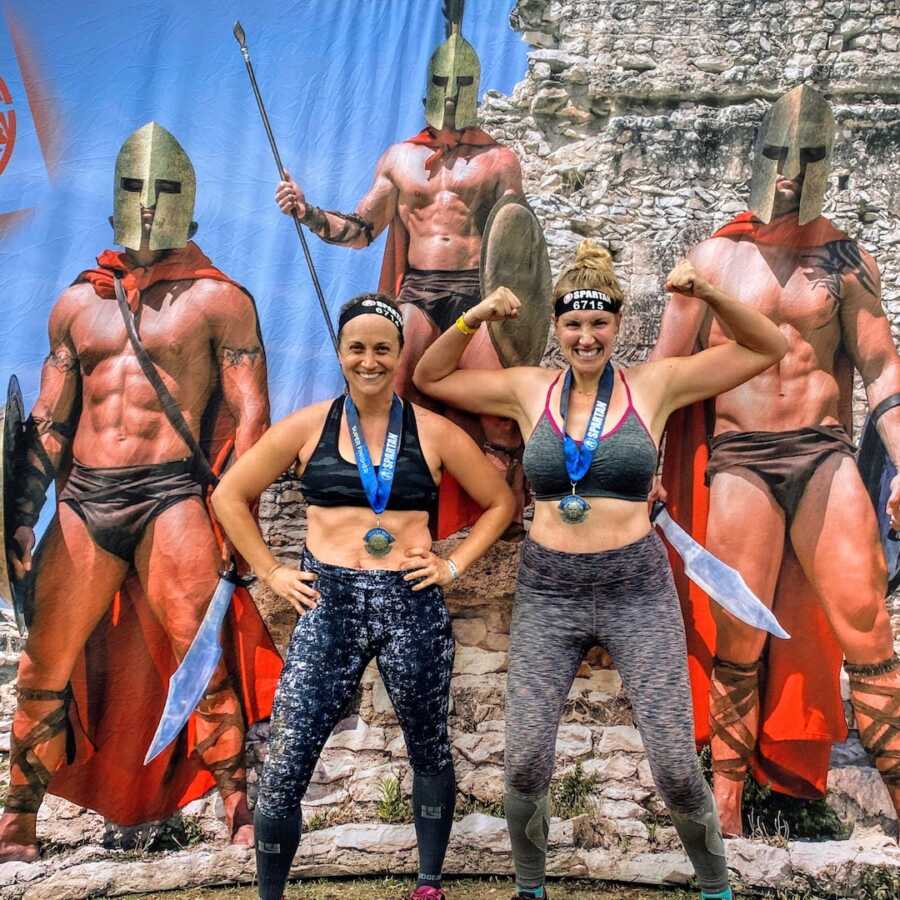 two women flexing in front of spartan background 
