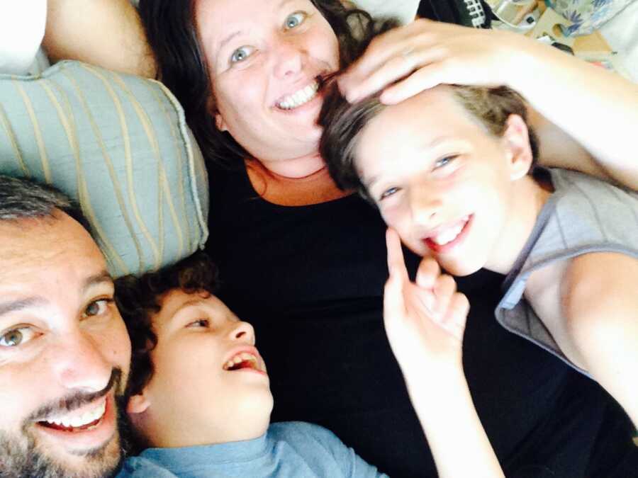 Parents and two boys lie on bed in family hug.