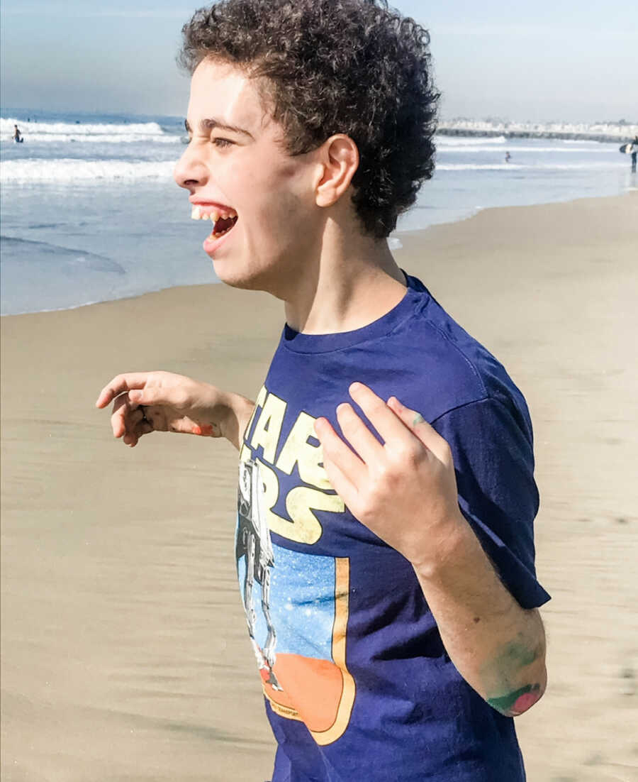 Teenager with special needs smiles happily at the beach, enjoying the waves.