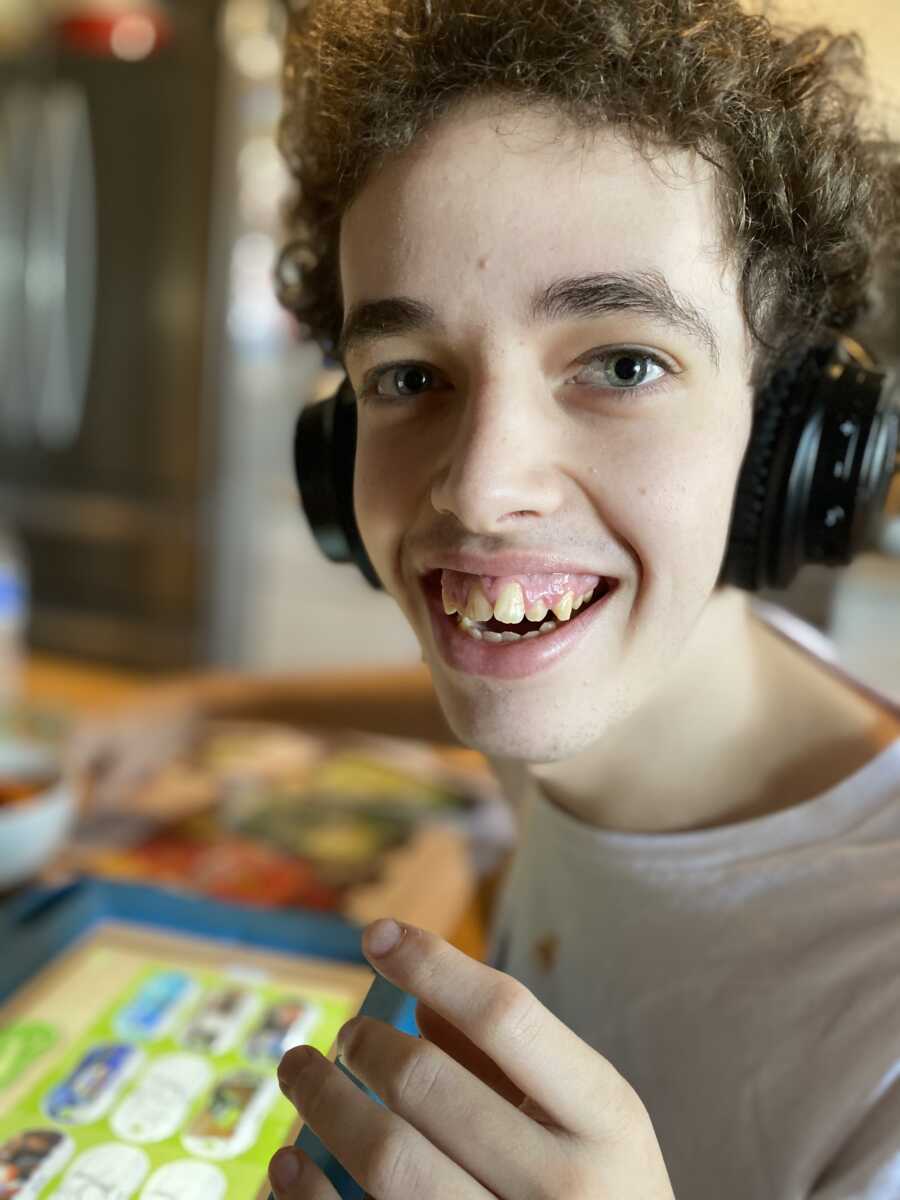 Teenager wearing headphones while sitting at the table shares big smile.