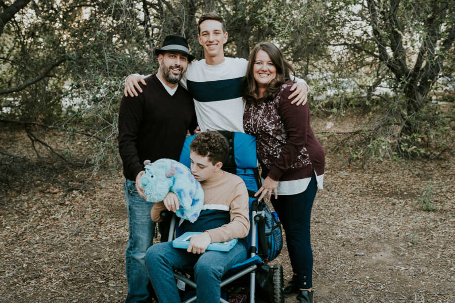 Family of four takes picture standing outside, with oldest son sitting in a wheelchair.