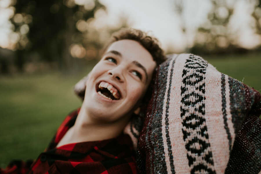 Teenager with SYNGAP1 shares big smile while resting his head on blanket.
