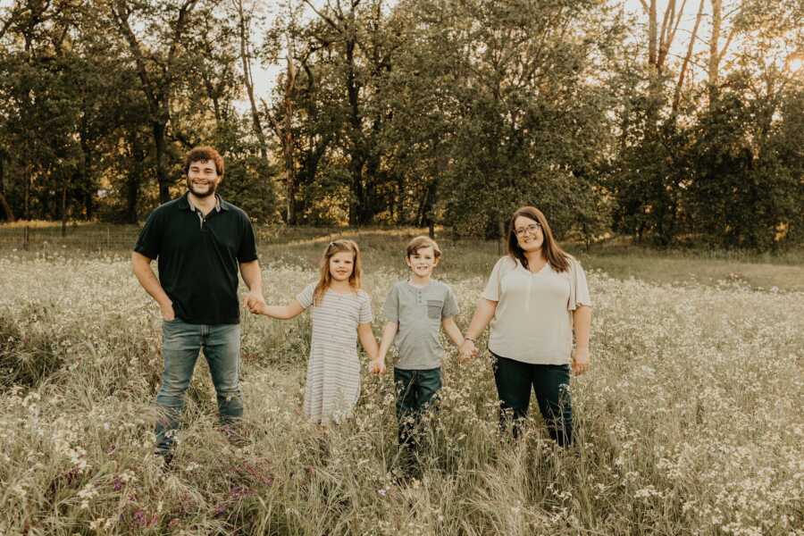 An adoptive family holds hands in a field