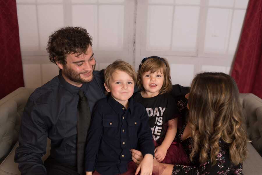 A mom and dad smile at their son and daughter on the couch