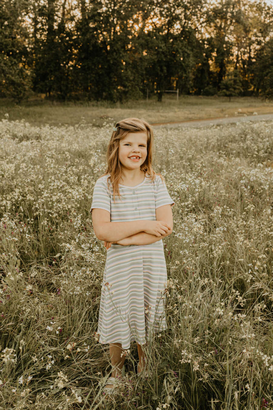 Adopted daughter with craniofacial differences stands with her arms crossed in a field