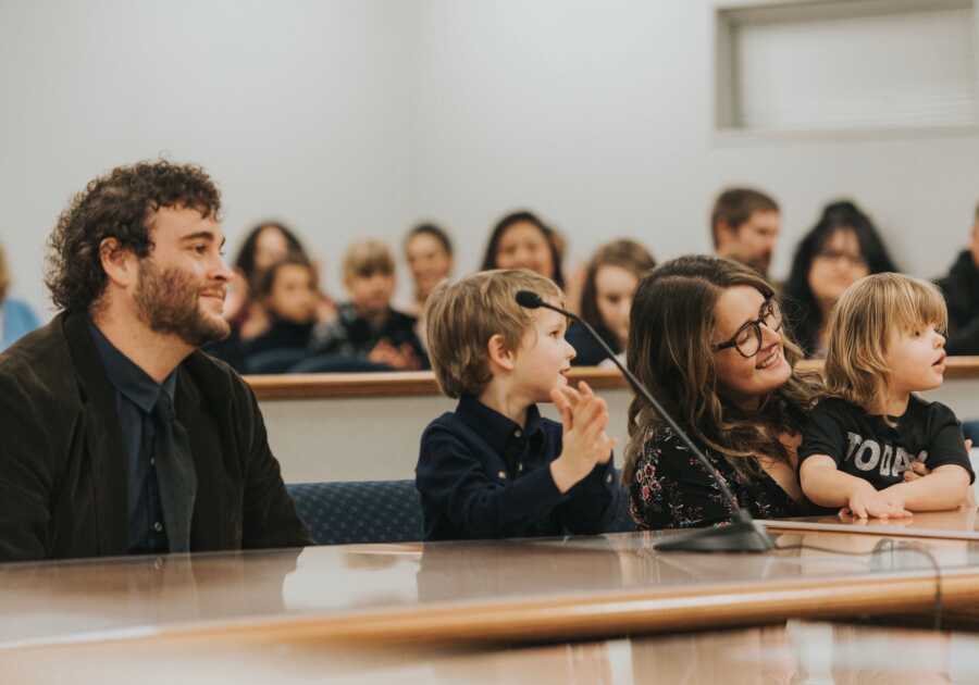 A family sits at court bench on adoption day while people clap behind them