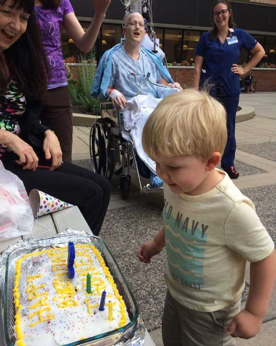 Toddler blows out birthday candles outside hospital where dad is receiving cancer treatment.