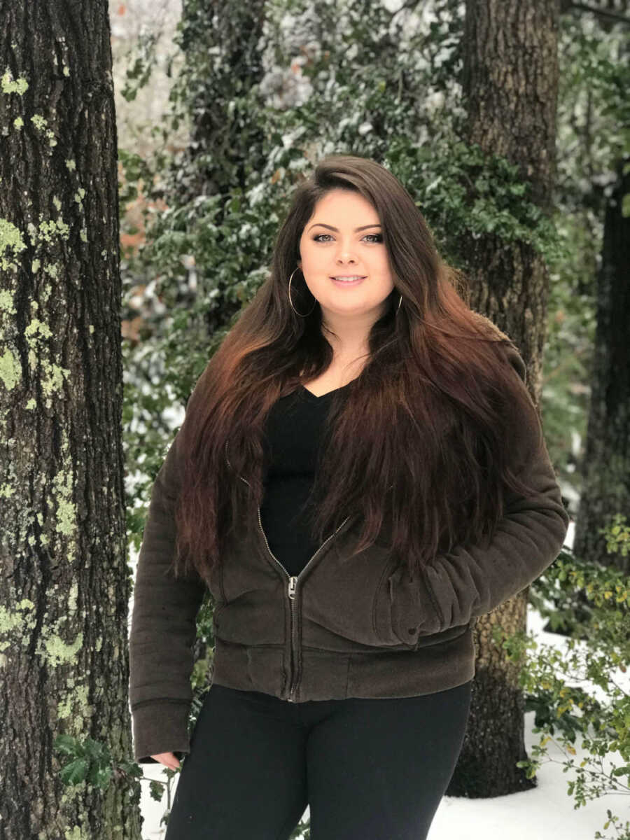 woman stands in woods with hand in pocket