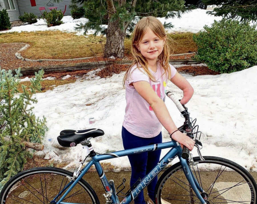 A young girl with one arm smiles holding a new bike