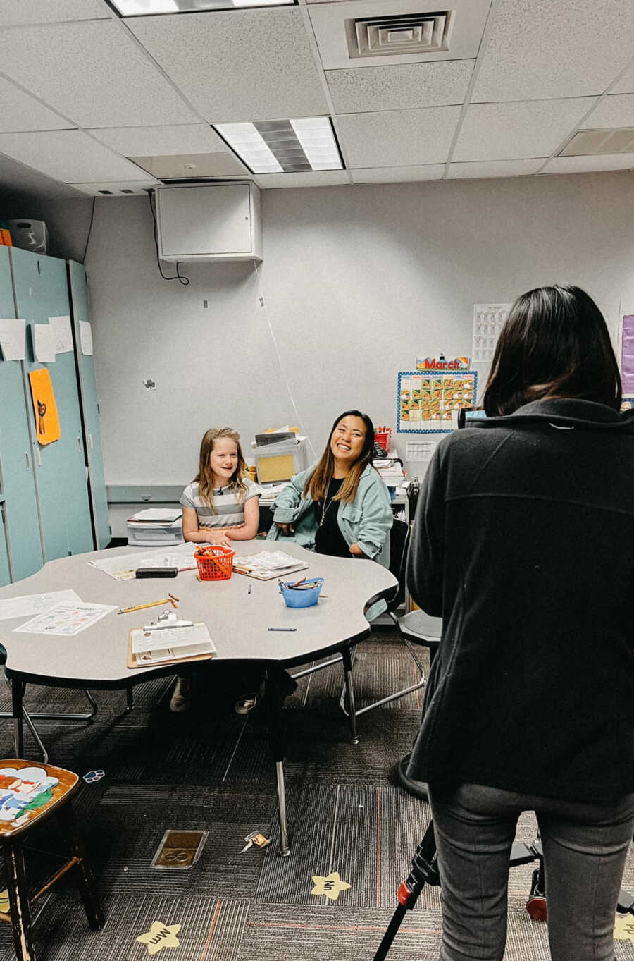 Elementary school teacher and student with one arm sit being filmed