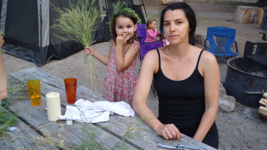 A woman and her daughter sit at a picnic table camping