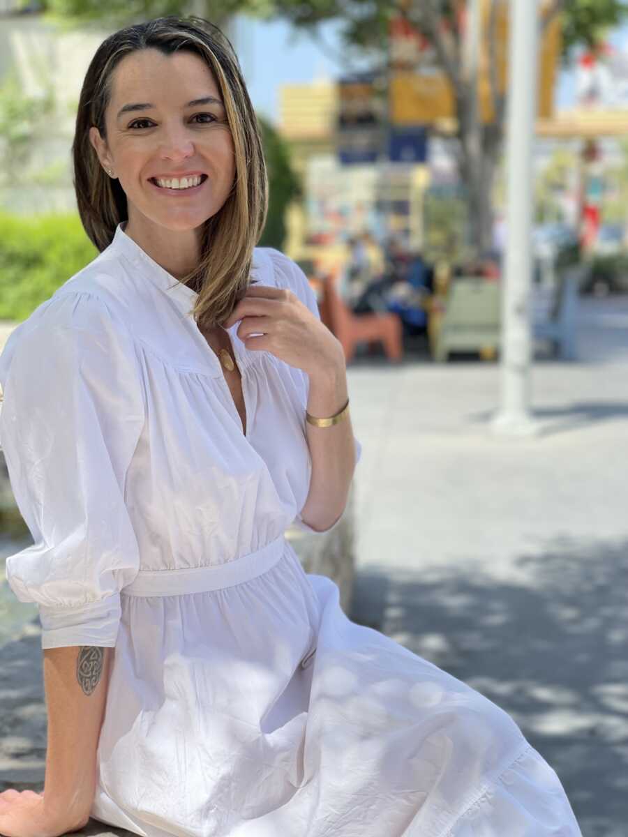 A woman in a white dress smiles at the camera