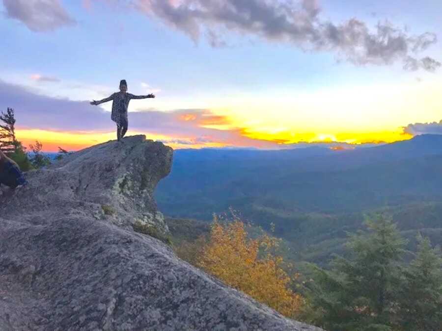 woman stands on the edge of a mountain looking at horizon