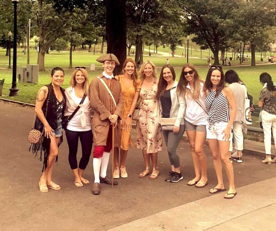 group of woman stand together on a girls trip posing with man dressed as old soldier