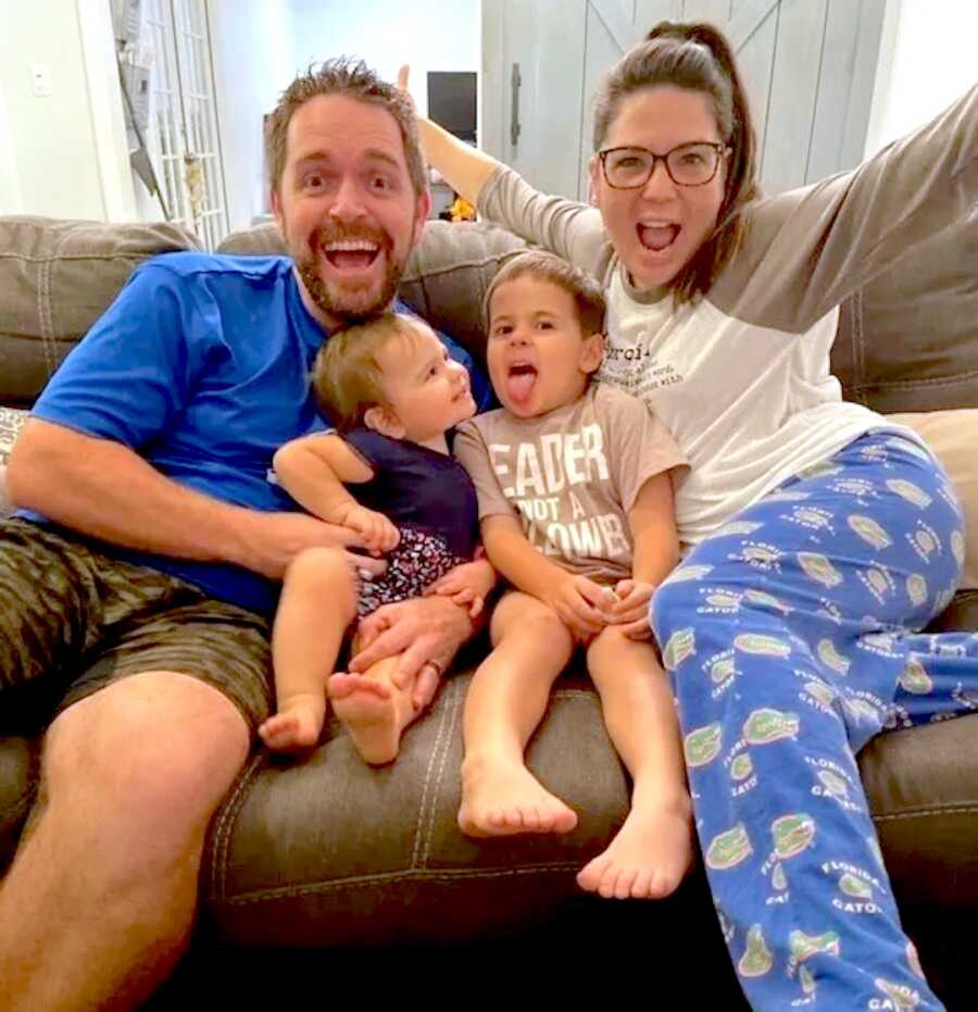 mom and dad sit on the couch in PJs with their two children