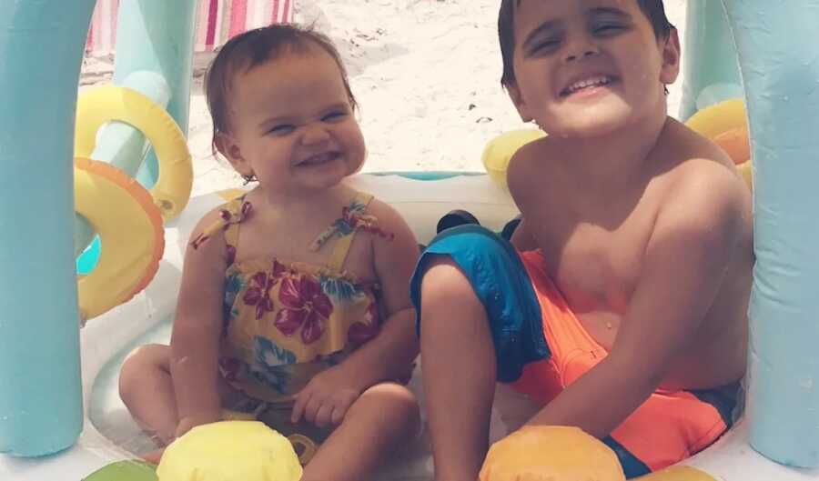 brother and sister sit together smiling while at the beach