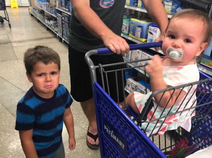 young boy upset at grocery store, sister sits in cart