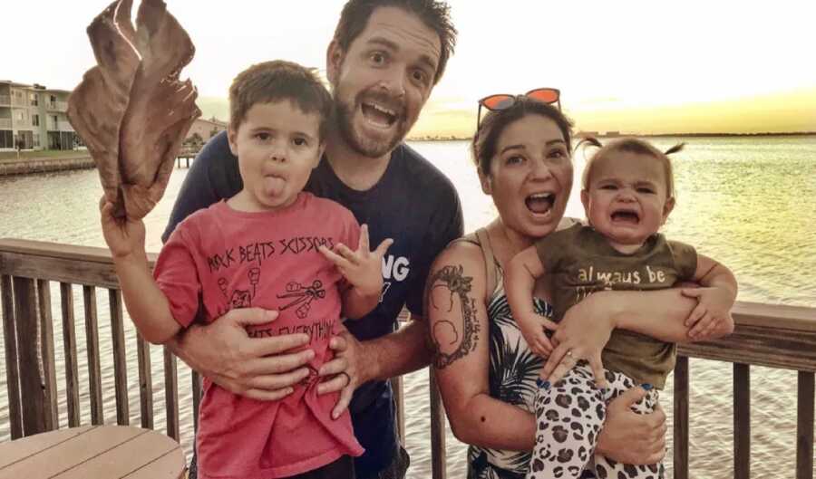 Young parents make crazy faces as they hold up their two toddlers.