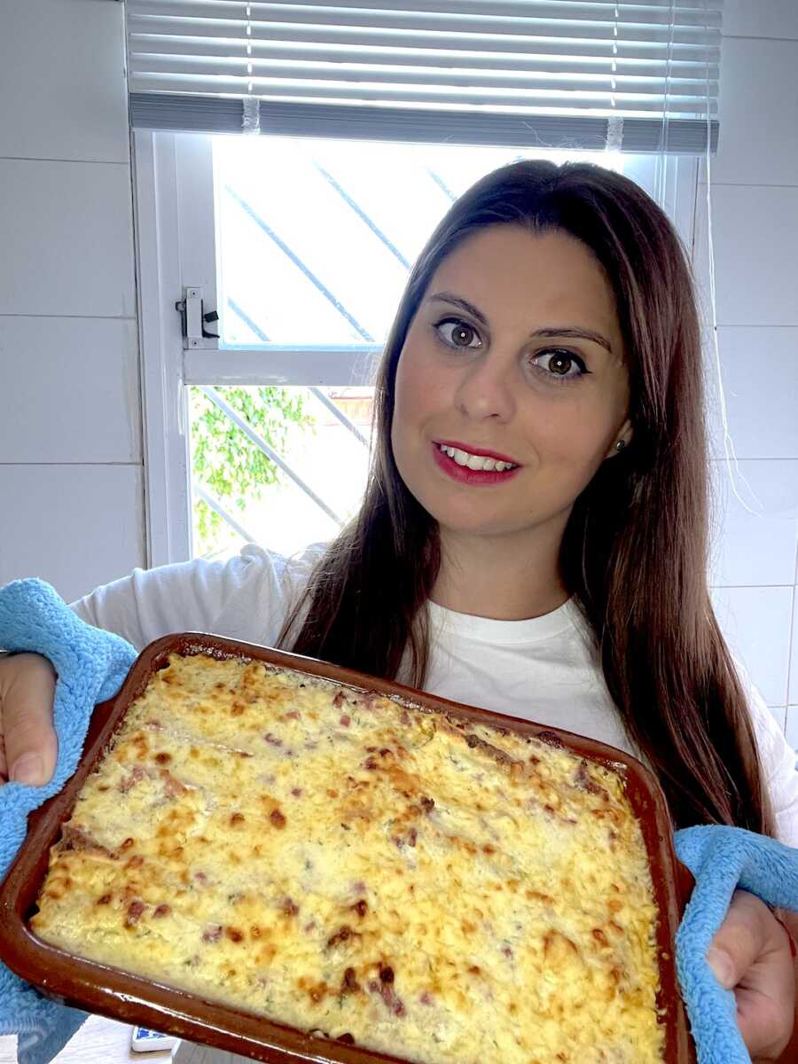 woman stands holding a pan of spanish canelones