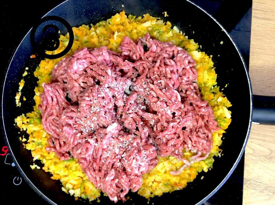 cooked down vegetables in pan with ground beef added on top
