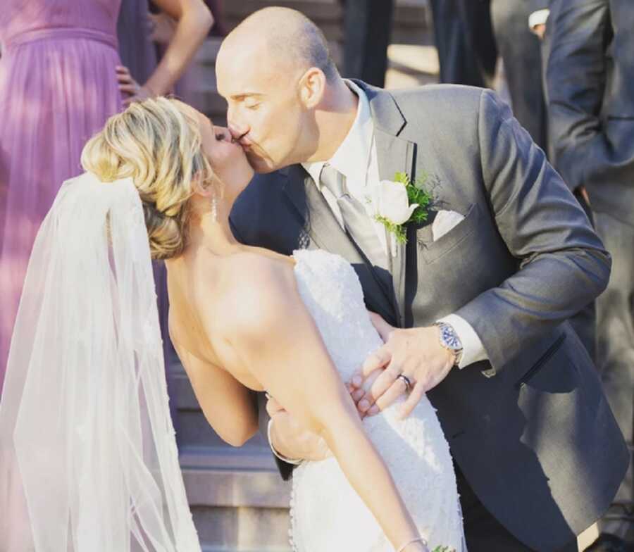 Groom dips bride and kisses her while pulling her close with his hands around her waist.