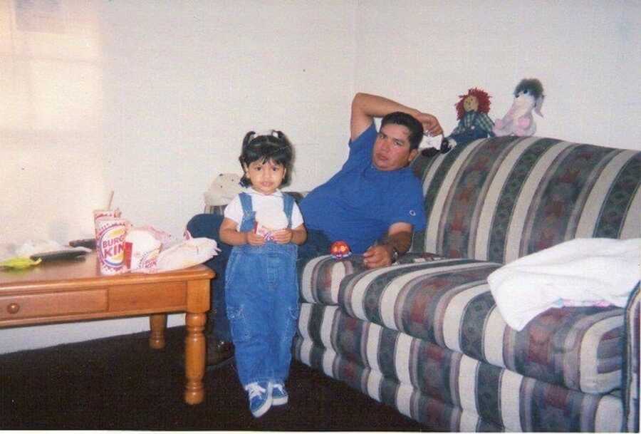 A man lays on a couch while his daughter stands next to him