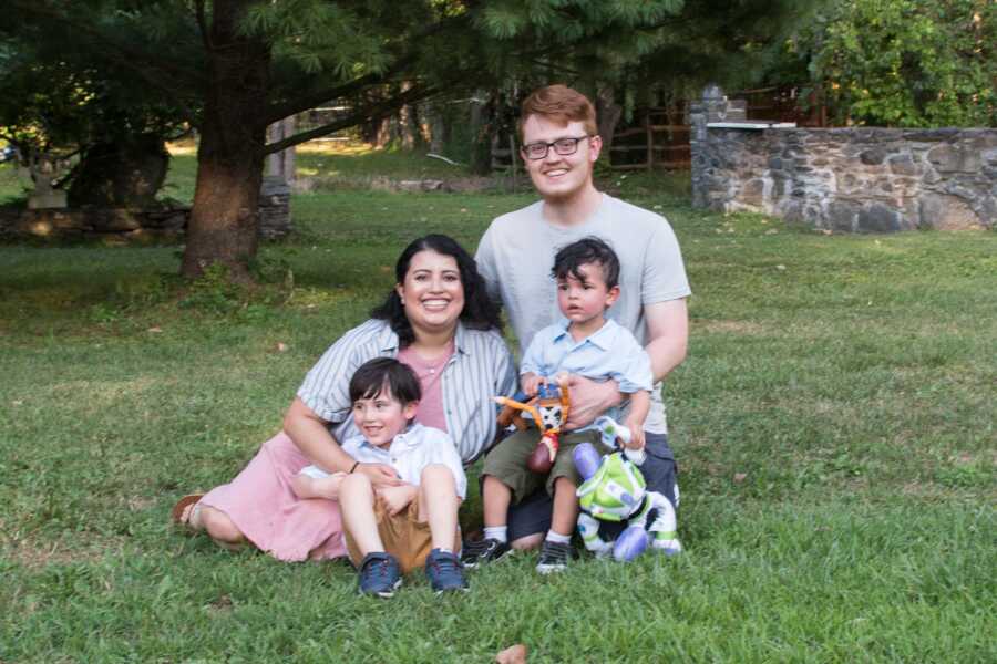 A family with two young boys pose with their dog outside 