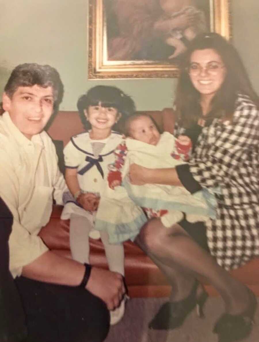 A family with a young girl and baby girl pose in their living room