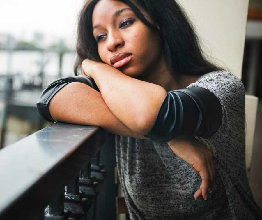 Depressed black woman rests head on arms while leaning on railing.