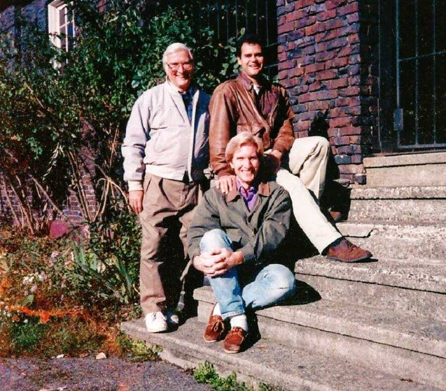 A man and his husband with his father on cement steps outdoors