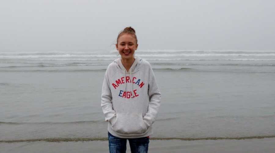 A young girl wearing a white sweatshirt stands by the water