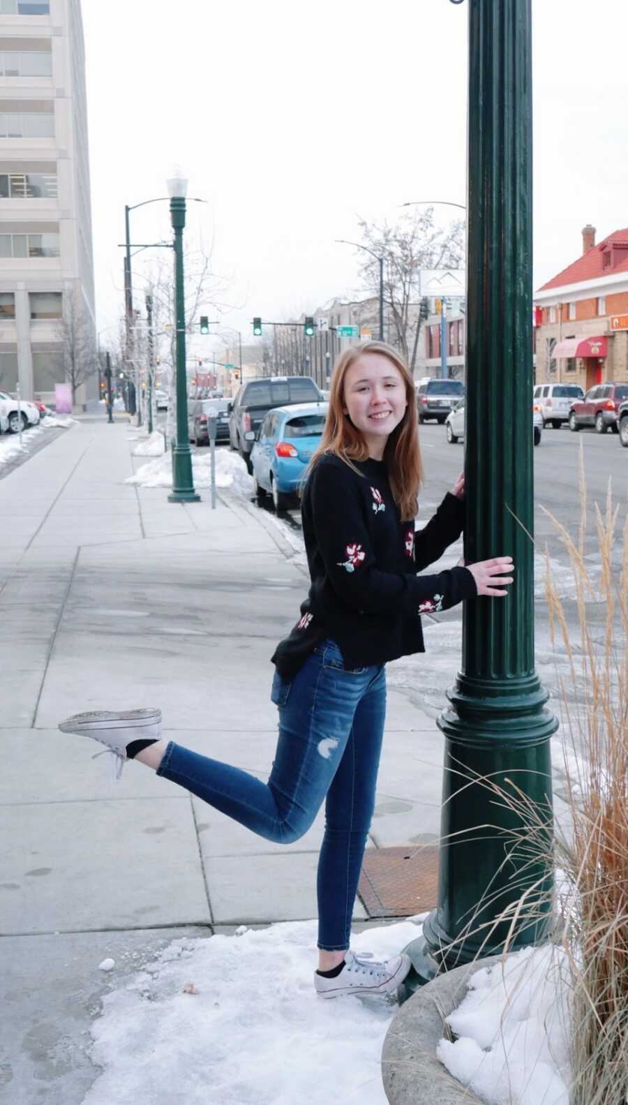 A young woman leans against a lamp post