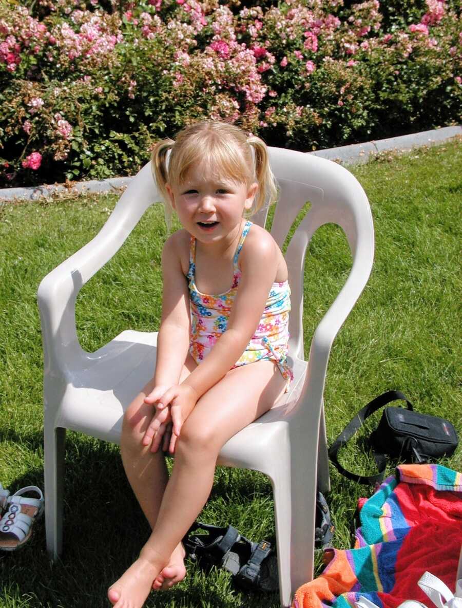 A young girl sits in a plastic chair wearing a bathing suit