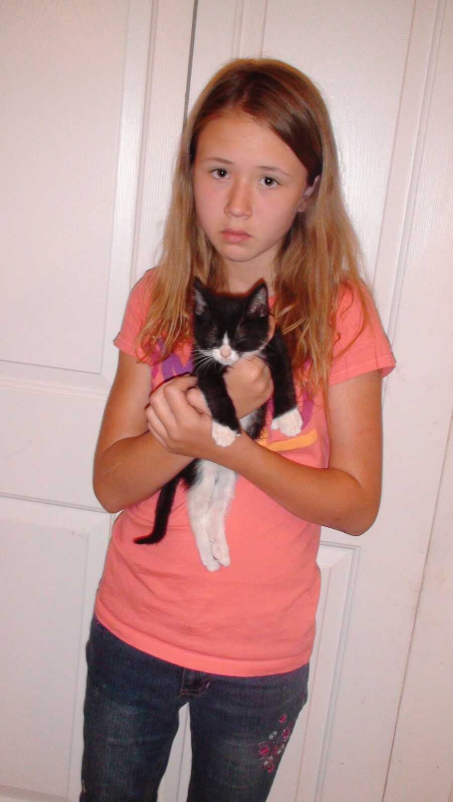A young girl holding a black and white kitten