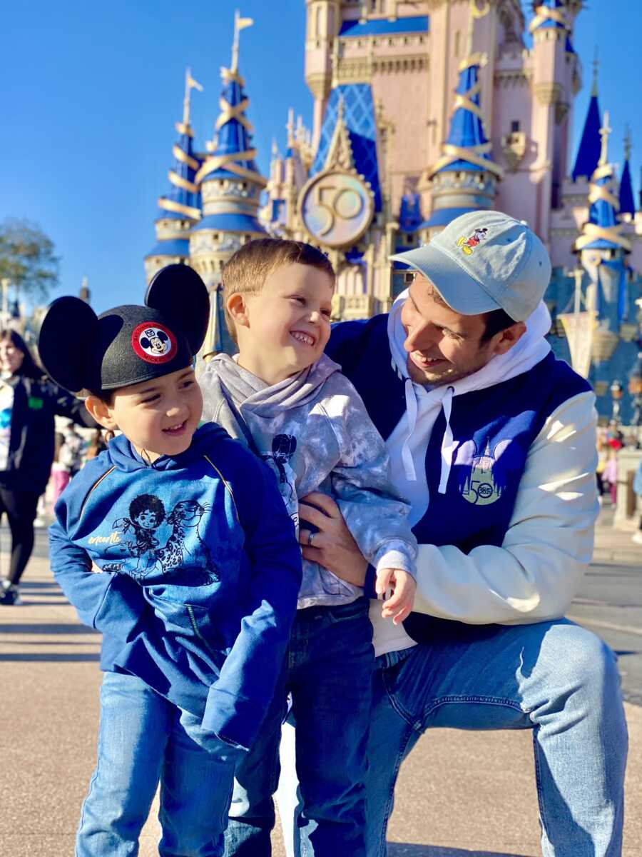 Dad crouches down next to two sons at Disney World.