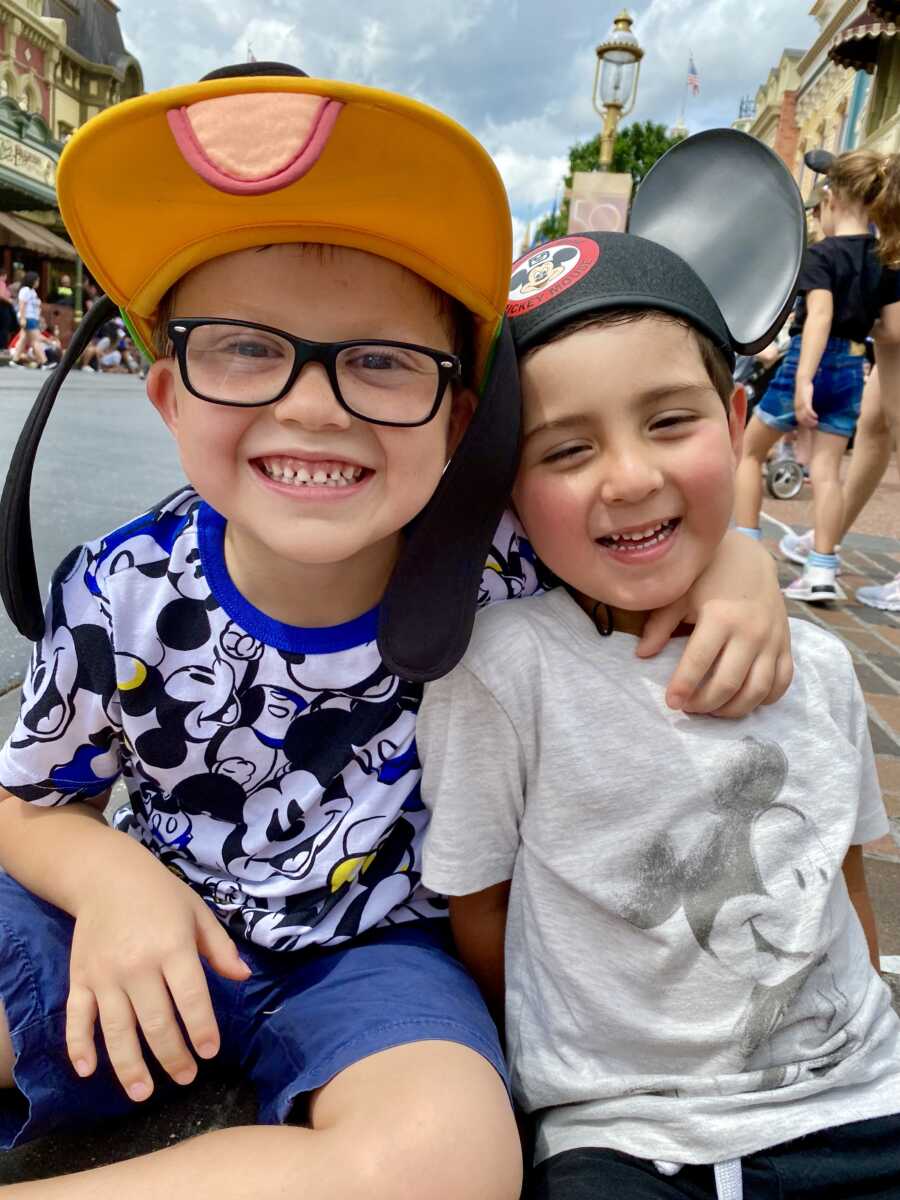 Adoptive brothers sit smiling together at Disney World, with older brother placing his arm around his younger brother.