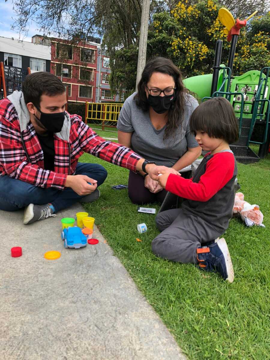 Couple sit on the ground and play with young Colombian boy they are adopting.