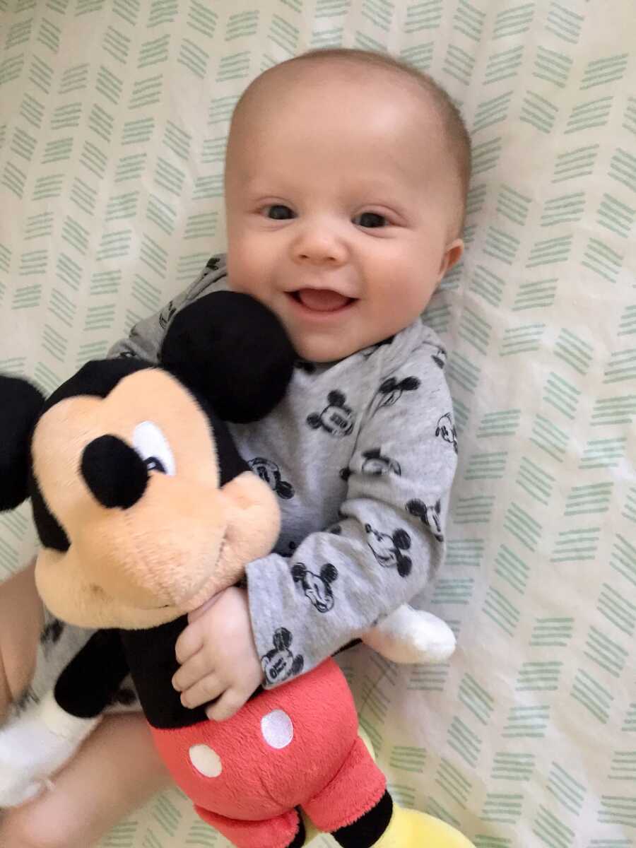 Baby boy lies on blanket and holds Mickey Mouse stuffed animal.