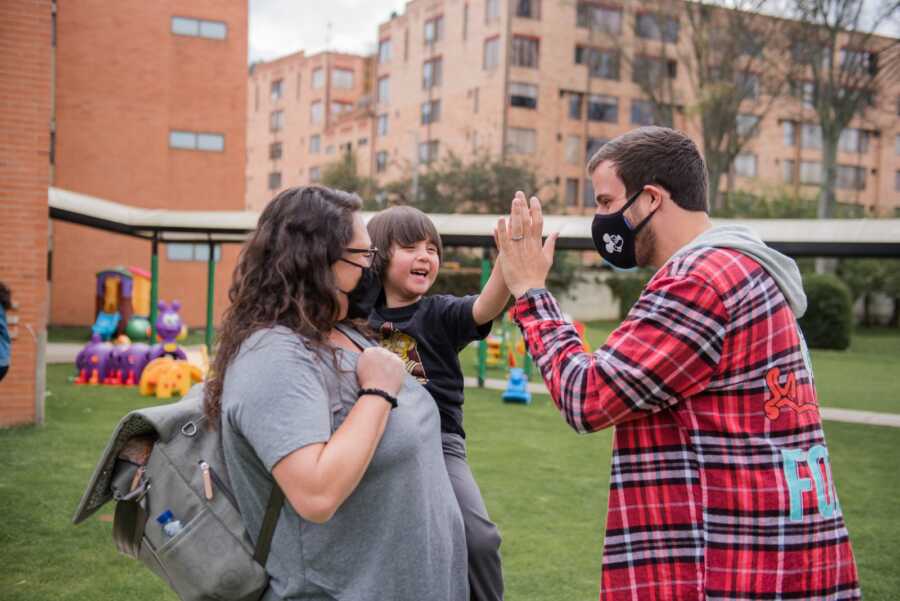 Mom holds Colombian boy as he high fives dad meeting him at the orphanage.