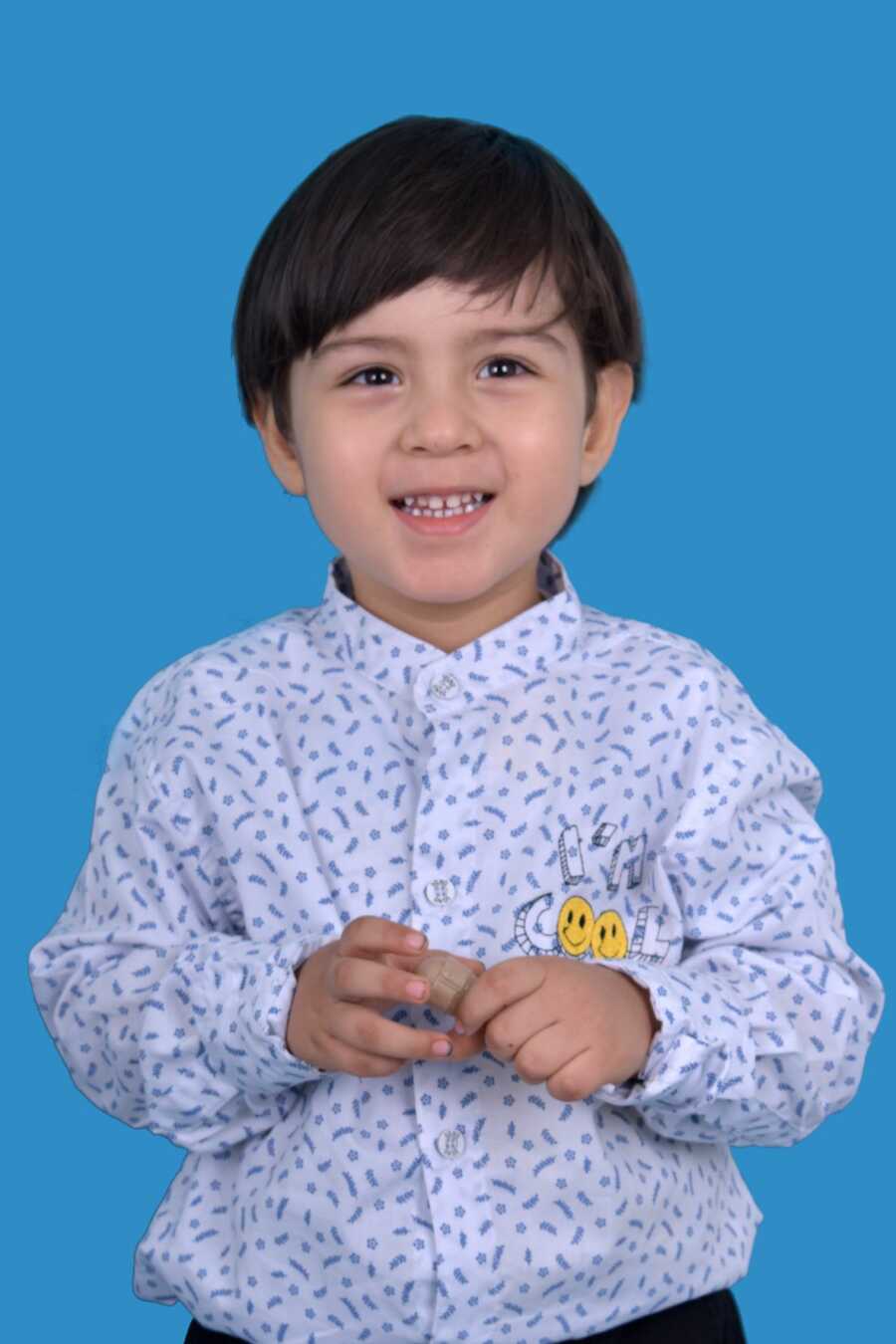 Young Colombian boy wearing white button up shirt smiles in front of blue backdrop.