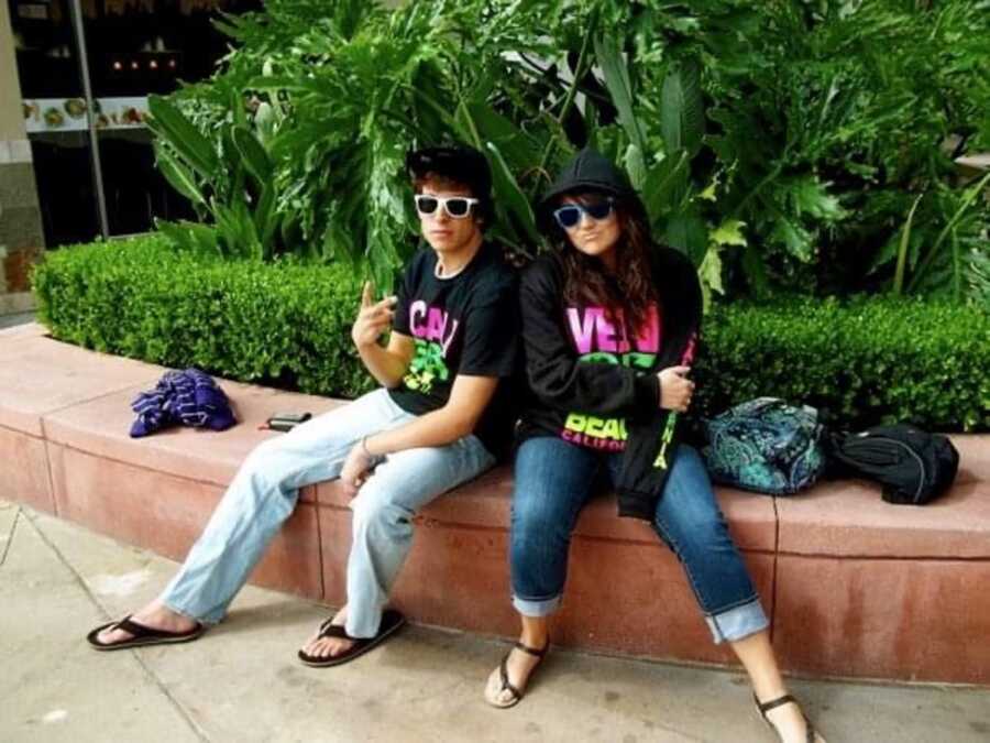 Young couple take picture sitting together wearing sunglasses and hats.